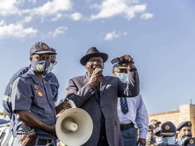 Bheki Cele speaking through a megaphone, surrounded by police.